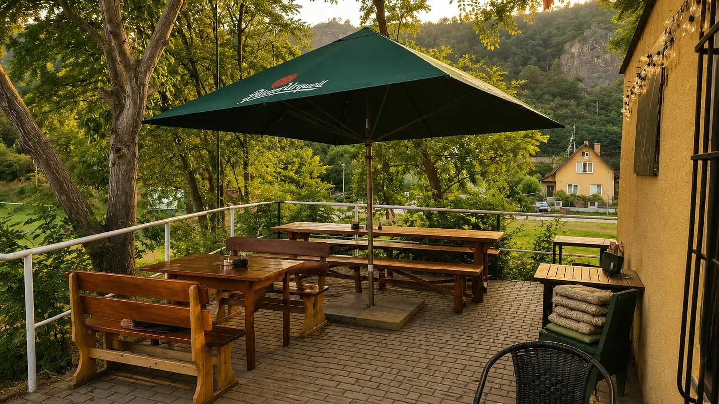 Außensitzplätze unter einem Sonnenschirm auf der Terrasse, hinter dem Geländer das Tal und ein Felshügel